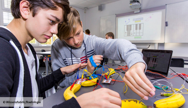 Zwei Jungs experimentieren mit Bananen und Kabeln im Unterricht