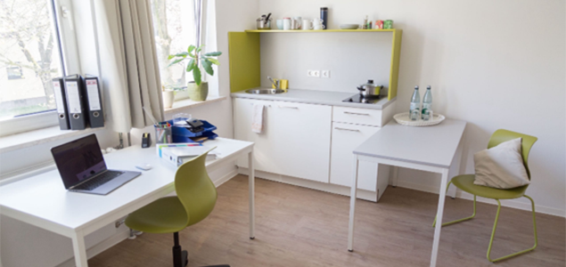 Blick in eine Wohnung mit Schreibtisch am Fenster und Tisch mit Stühlen
